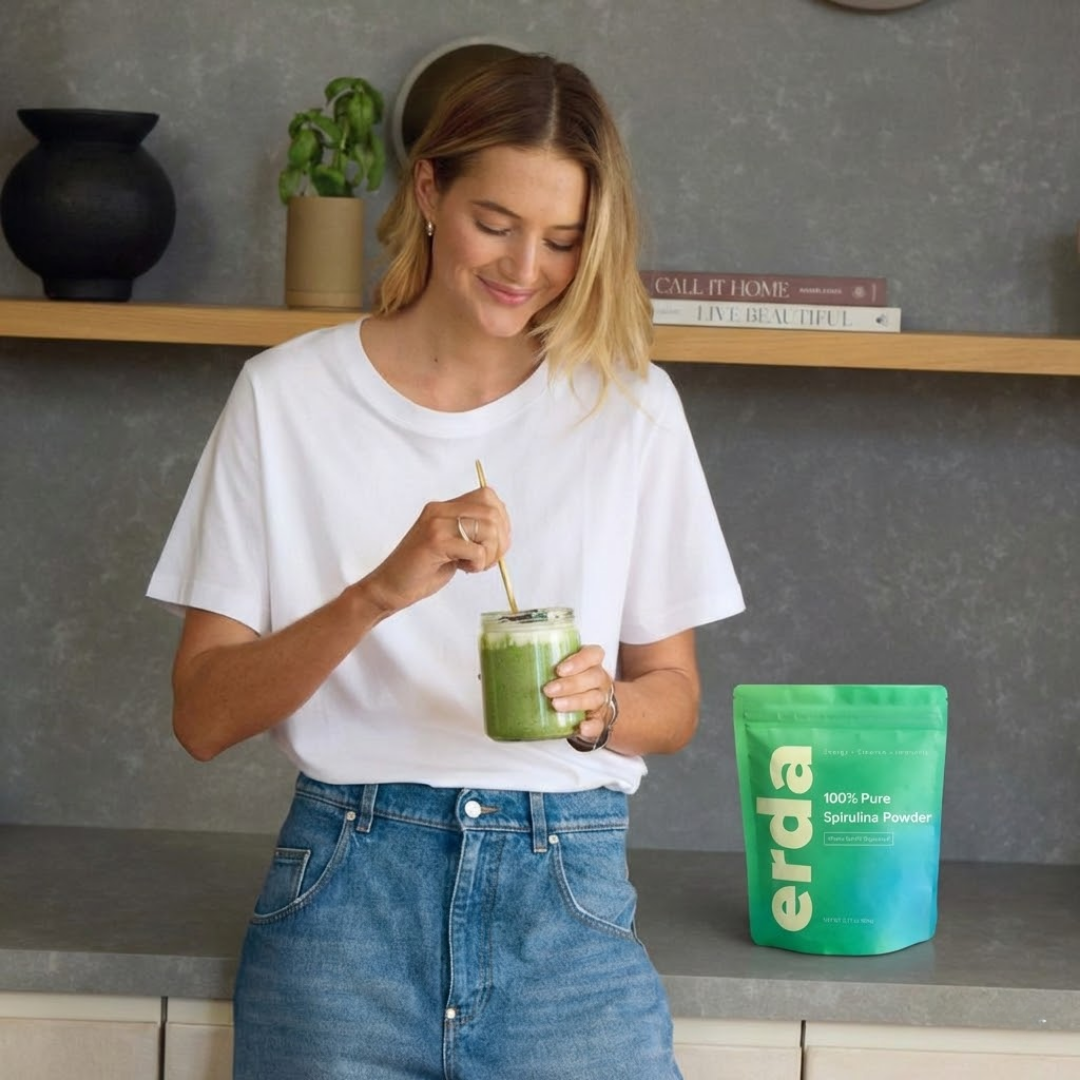 Woman stirring a green smoothie with a package of 'erda' powder in the background.